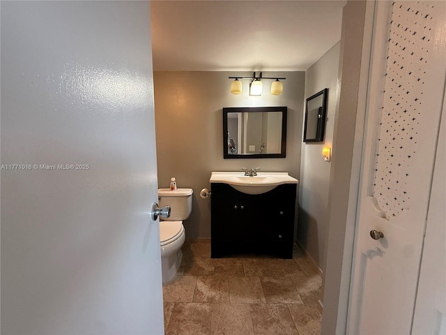 bathroom with baseboards, toilet, stone finish floor, and vanity