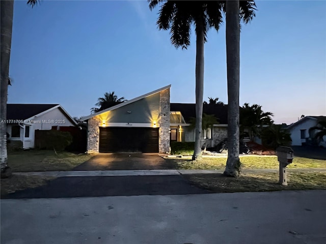 view of front facade with stucco siding, an attached garage, driveway, and stone siding