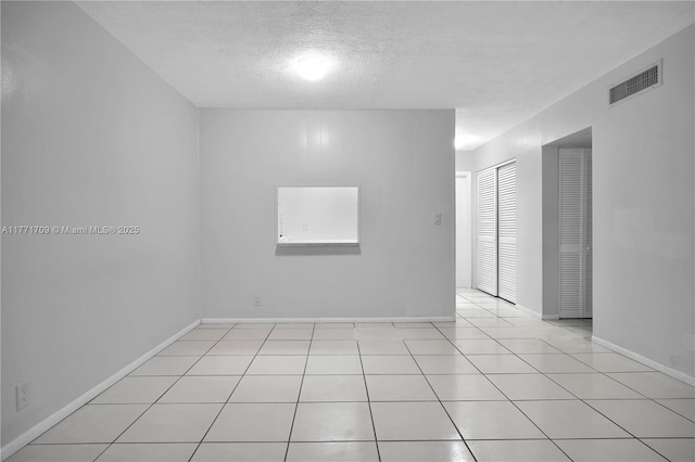 spare room featuring a textured ceiling, visible vents, baseboards, and light tile patterned floors