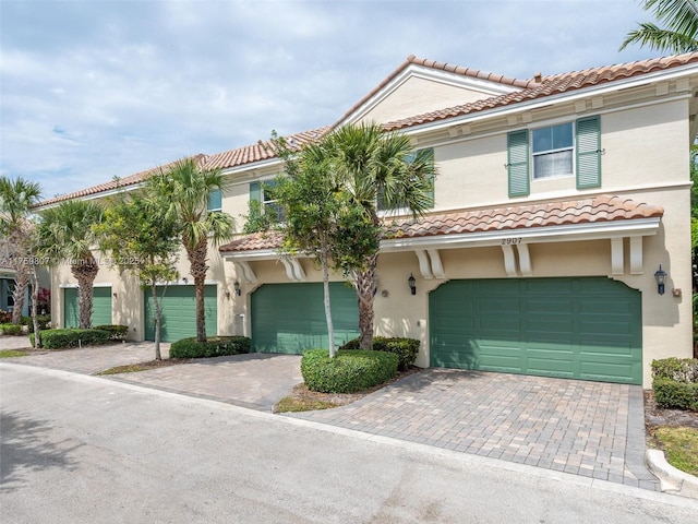 mediterranean / spanish-style home with a tiled roof, a garage, stucco siding, and decorative driveway