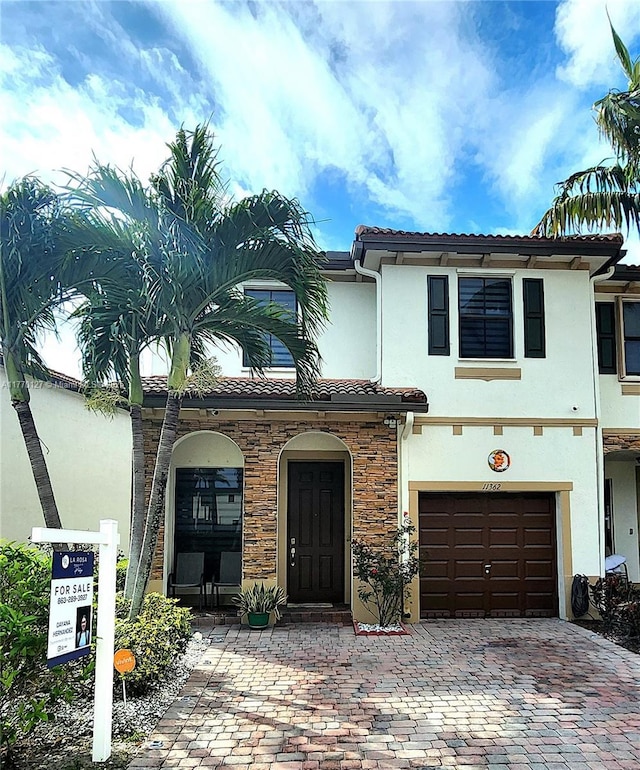 view of front of house featuring stucco siding, stone siding, a tiled roof, decorative driveway, and a garage