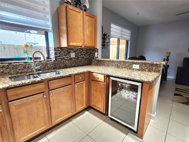 kitchen featuring light tile patterned flooring, backsplash, a sink, a peninsula, and beverage cooler