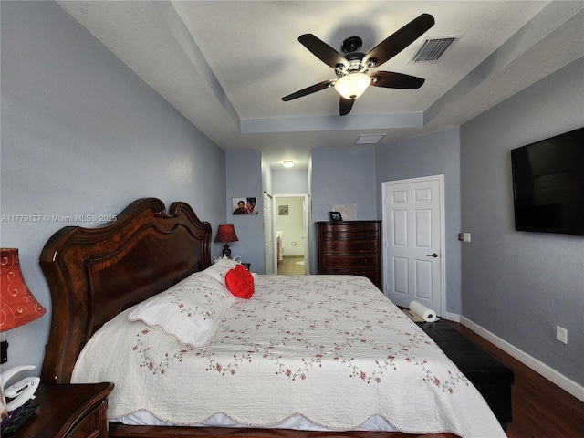 bedroom featuring baseboards, a raised ceiling, ensuite bath, visible vents, and wood finished floors
