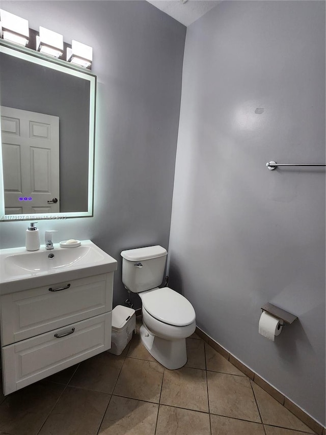 half bath featuring tile patterned floors, toilet, baseboards, and vanity