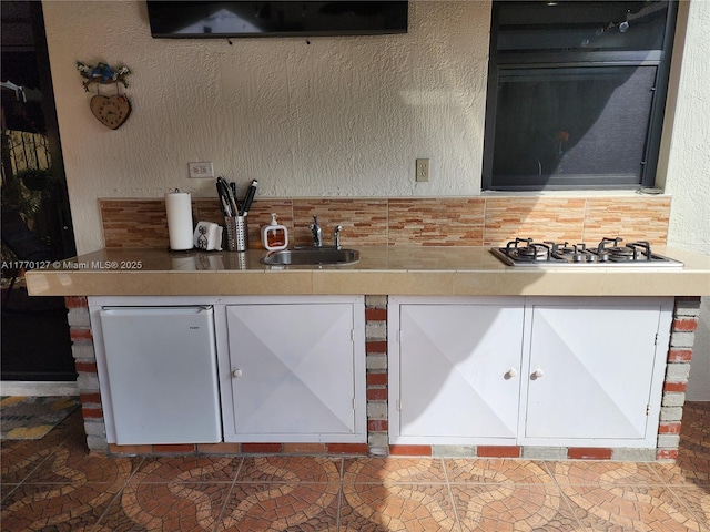 kitchen featuring a textured wall, stainless steel gas cooktop, a sink, and fridge