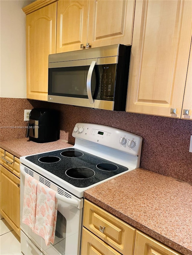 kitchen featuring light brown cabinets, stainless steel microwave, electric stove, backsplash, and light countertops