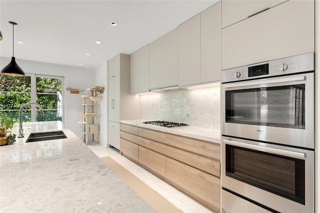 kitchen featuring a sink, tasteful backsplash, light stone countertops, stainless steel double oven, and modern cabinets