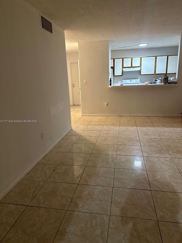 spare room with a textured ceiling, visible vents, tile patterned flooring, and baseboards