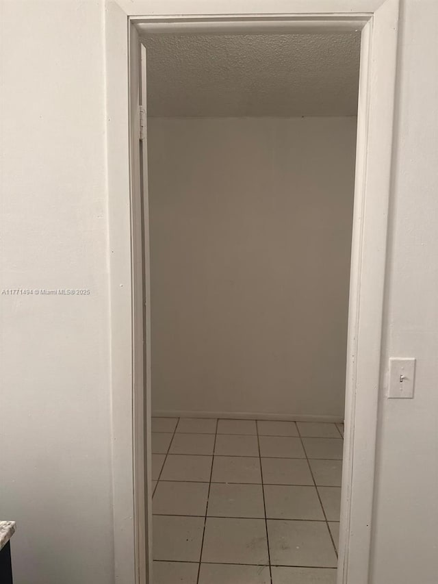 hallway with a textured ceiling and light tile patterned floors