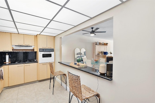 kitchen with black stovetop, range hood, light tile patterned flooring, dark countertops, and oven