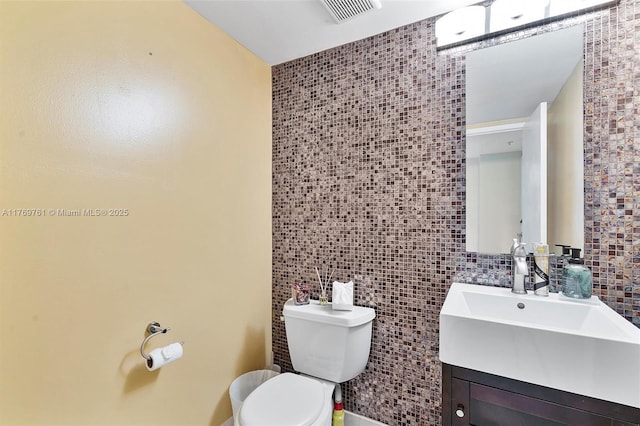 bathroom with toilet, tile walls, vanity, and visible vents