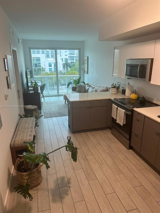 kitchen featuring light countertops, light wood-type flooring, stainless steel microwave, a peninsula, and range with electric cooktop
