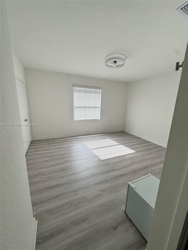 empty room featuring baseboards, wood finished floors, and a textured ceiling