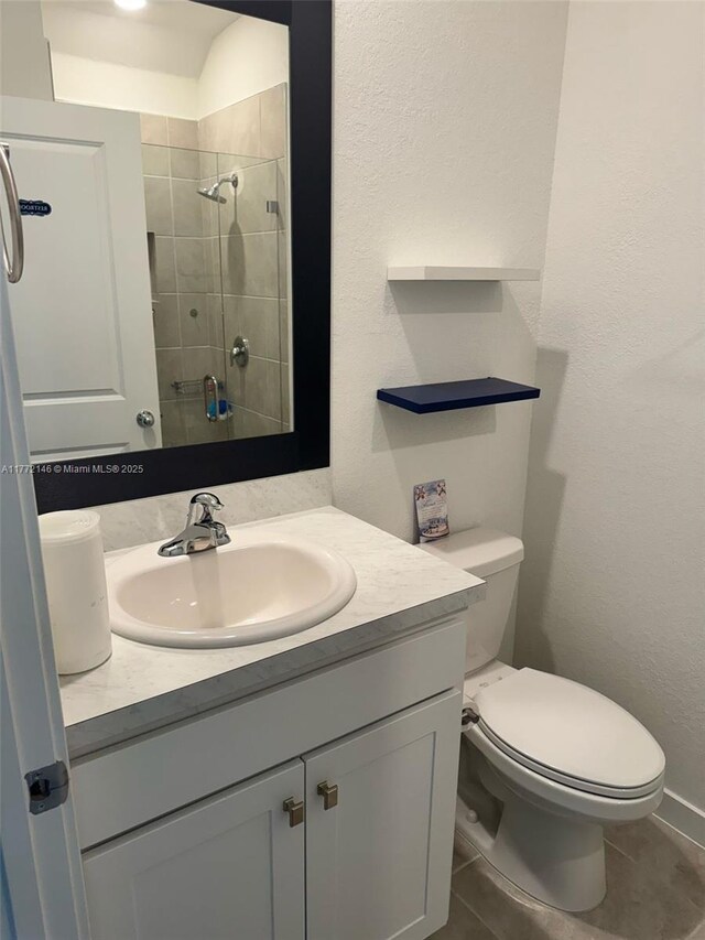 bathroom with tile patterned flooring, vanity, toilet, a textured wall, and tiled shower