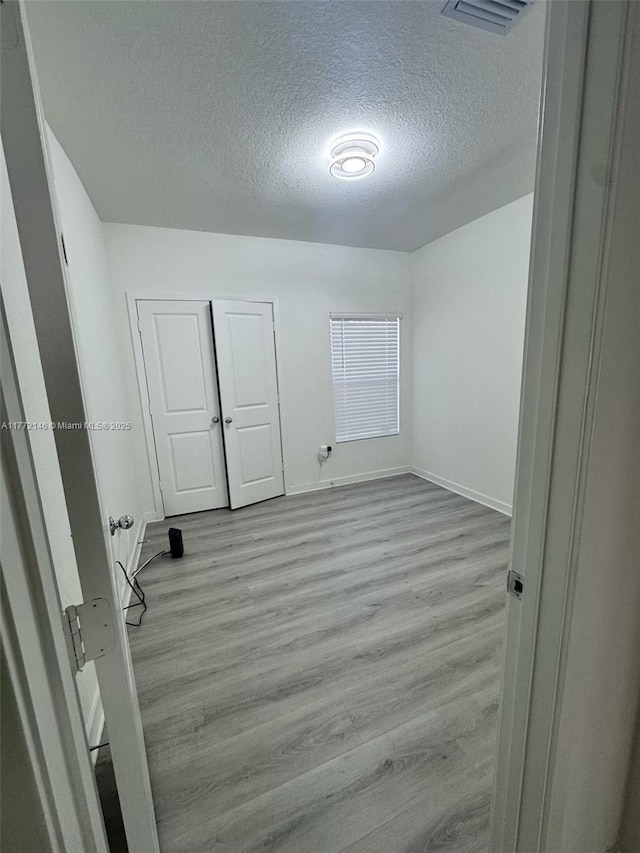 unfurnished bedroom featuring visible vents, baseboards, light wood finished floors, and a textured ceiling