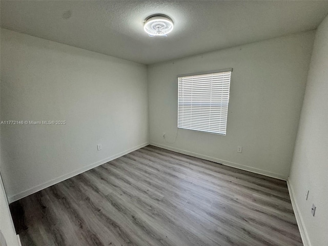 unfurnished room featuring a textured ceiling, baseboards, and wood finished floors