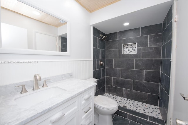 full bath featuring a wainscoted wall, toilet, tiled shower, vanity, and visible vents