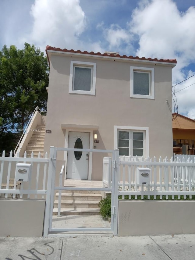 view of front facade with stucco siding, a gate, a fenced front yard, and a tiled roof