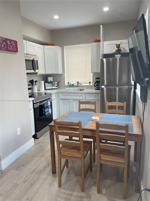 kitchen with light countertops, decorative backsplash, a sink, light wood finished floors, and appliances with stainless steel finishes
