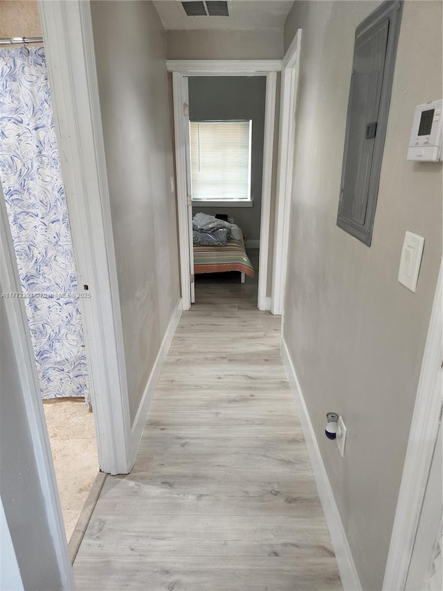 hall featuring electric panel, baseboards, visible vents, and light wood-style floors