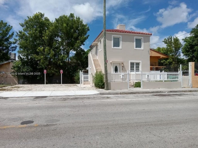 view of front of property with a tiled roof, a chimney, stairs, a fenced front yard, and stucco siding