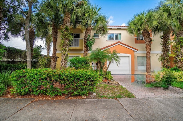 mediterranean / spanish home featuring stucco siding, a garage, a tiled roof, and decorative driveway