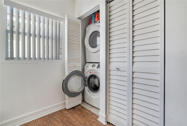 laundry area with stacked washer and dryer, baseboards, wood finished floors, and laundry area