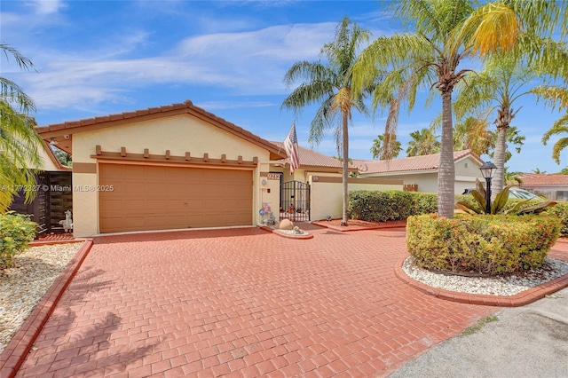 ranch-style house featuring a gate, decorative driveway, a tiled roof, an attached garage, and stucco siding