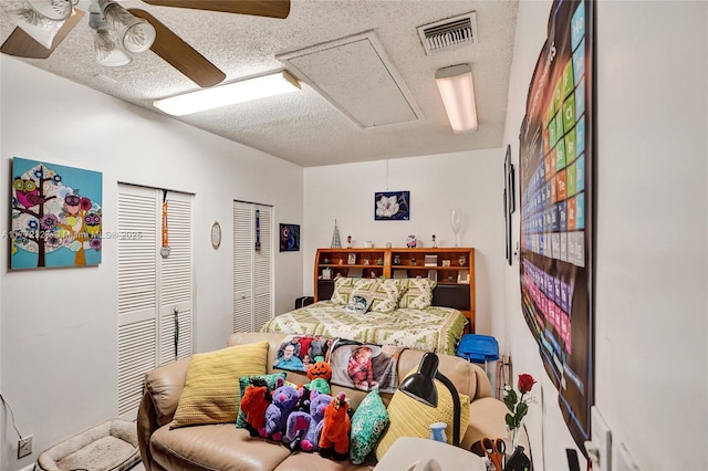 bedroom featuring attic access, a textured ceiling, visible vents, a ceiling fan, and two closets