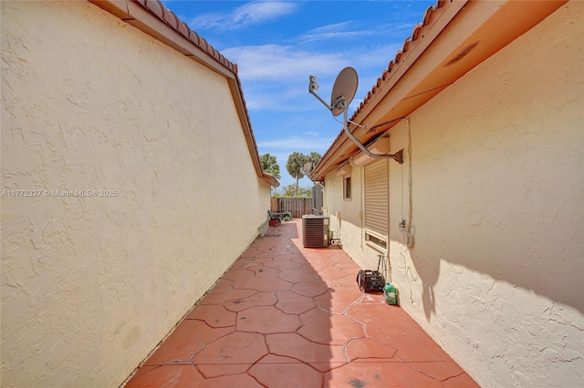 view of property exterior featuring a tile roof, central AC unit, fence, a patio area, and stucco siding