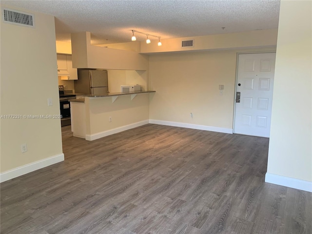 unfurnished living room with a textured ceiling, dark wood-style flooring, and baseboards