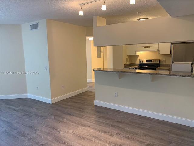 kitchen featuring stainless steel electric range oven, under cabinet range hood, a breakfast bar area, a textured ceiling, and white cabinetry