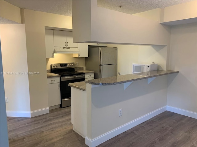 kitchen with white appliances, a peninsula, dark wood-type flooring, under cabinet range hood, and a textured ceiling
