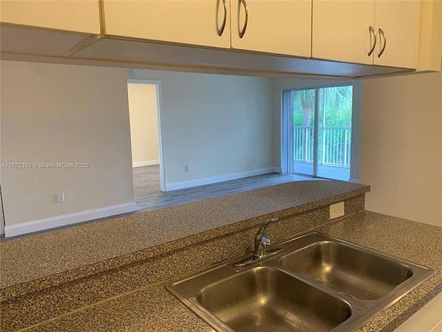 kitchen view of a sink, dark countertops, white cabinetry, and baseboards