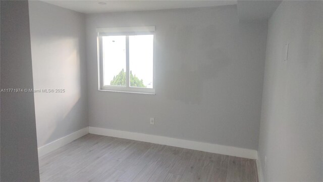 spare room with baseboards and light wood-type flooring