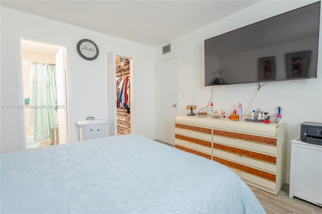 bedroom featuring a textured ceiling, visible vents, a walk in closet, and light wood-type flooring