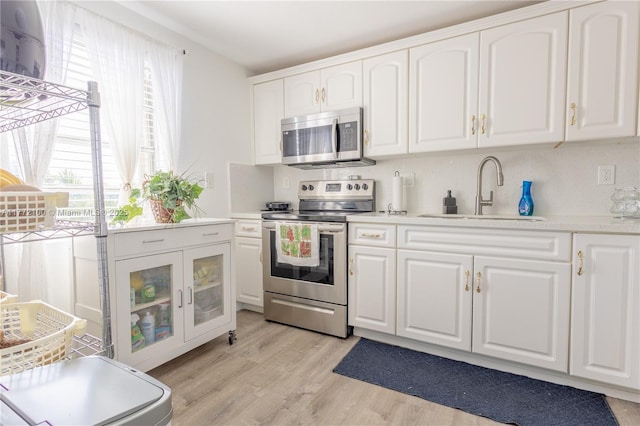kitchen with light countertops, light wood-style flooring, stainless steel appliances, white cabinetry, and a sink