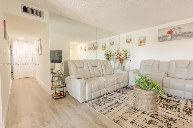 living area featuring baseboards, visible vents, wood finished floors, and a textured ceiling