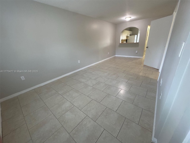 tiled empty room featuring baseboards and arched walkways