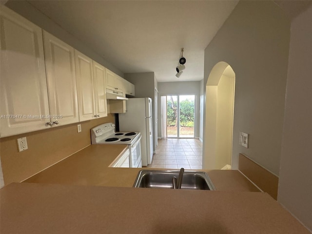 kitchen featuring white appliances, light tile patterned floors, under cabinet range hood, a sink, and arched walkways