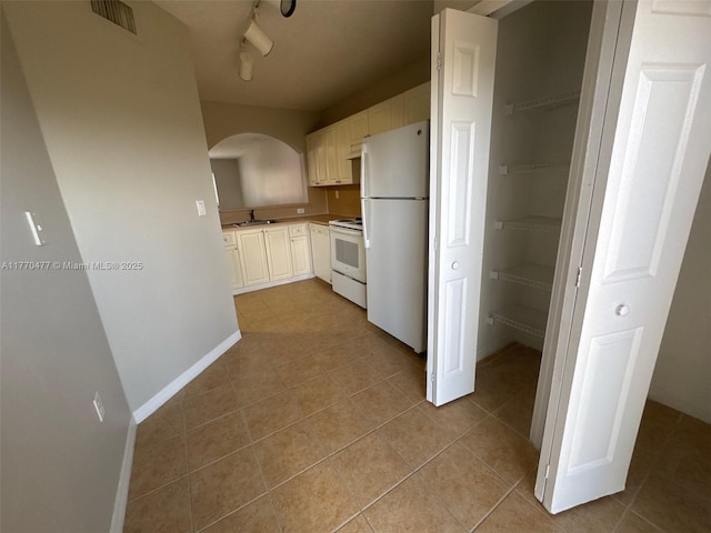 kitchen featuring a sink, baseboards, light tile patterned floors, white appliances, and arched walkways