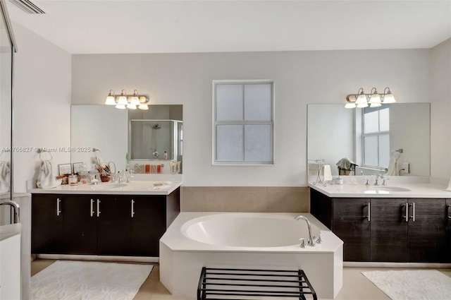 full bath with visible vents, a sink, two vanities, a stall shower, and a garden tub