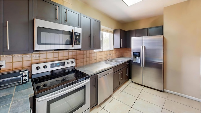 kitchen with stainless steel appliances, backsplash, light countertops, a sink, and light tile patterned flooring