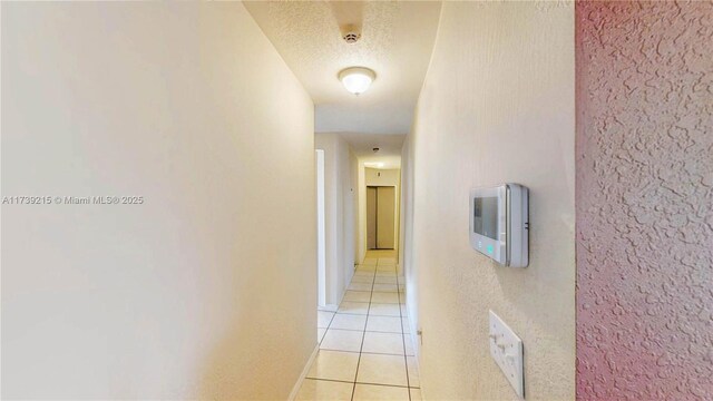 hall with a textured ceiling and light tile patterned floors