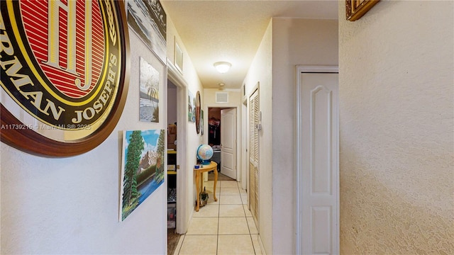 hallway featuring a textured wall, visible vents, and light tile patterned flooring