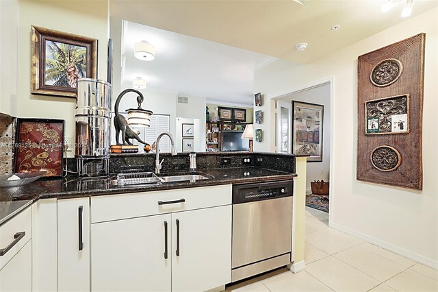 kitchen featuring dishwasher, dark stone countertops, light tile patterned floors, white cabinets, and a sink
