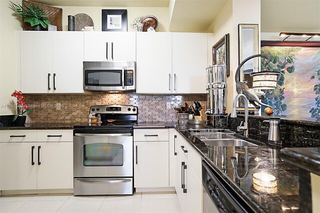 kitchen with appliances with stainless steel finishes, dark stone countertops, white cabinets, and a sink