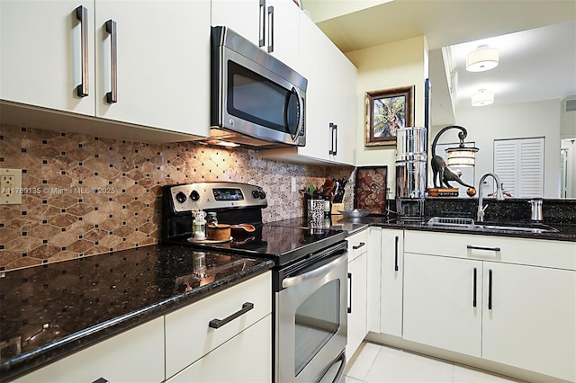 kitchen featuring stainless steel appliances, a sink, dark stone countertops, and light tile patterned flooring