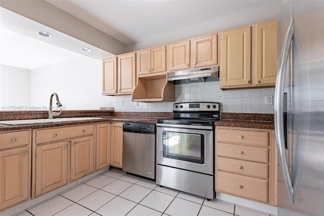 kitchen featuring stainless steel appliances, light brown cabinetry, under cabinet range hood, decorative backsplash, and a sink
