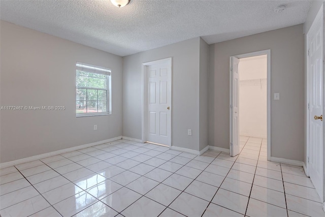 unfurnished bedroom featuring light tile patterned floors, a closet, a walk in closet, and baseboards